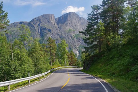 A winding road leads through thick forests with large mountains in the background, Eikesdalen.
