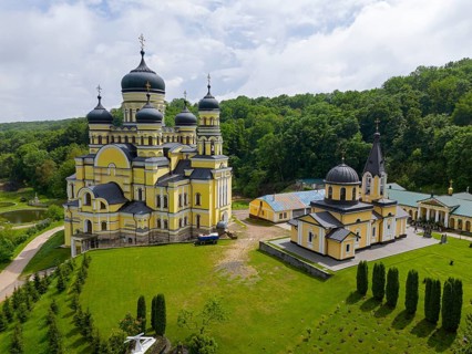 Orthodox monastery with yellow walls and domes, nestled in green landscape, aerial view, Hîncu