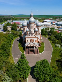 Front view of an Orthodox church with several domes and entrance area surrounded by green trees,