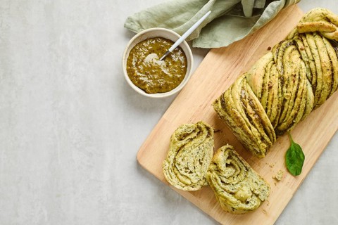 Baked homemade savoury babka plaited bread loaf flavoured with pesto on wooden bread board