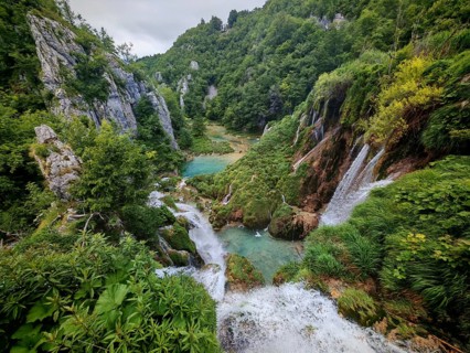Picturesque waterfalls flowing into a river surrounded by lush vegetation and rocky cliffs,