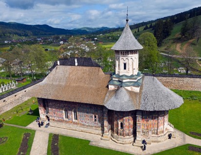 Close-up of a church with painted walls standing on a green area against a mountain backdrop,