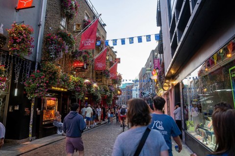Tourists stroll down a paved street illuminated by shops in the evening, Dublin, Ireland