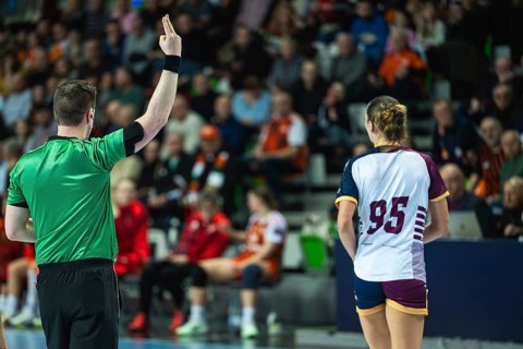 A handball referee showing a two-minute suspension sign with fingers during a high-stakes