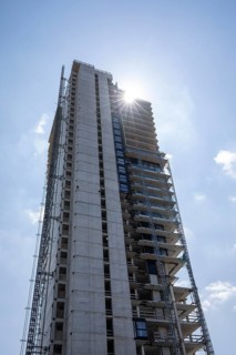 Daytime vertical low-angle view looking up at the high-rise shell and construction site of the SLT
