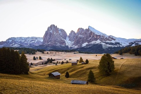 Snow-capped mountains with colorful meadows and wooden huts in the foreground, view over the