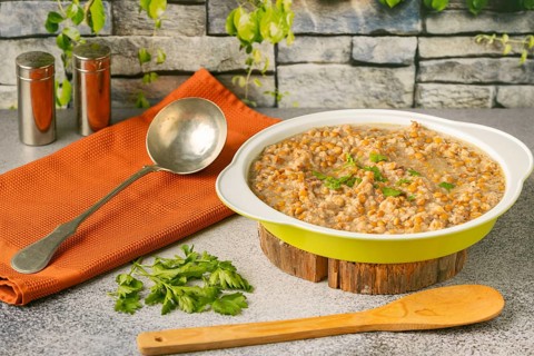 Lentils with bacon in a bowl with a ladle next to it, rustic stone wall in the background