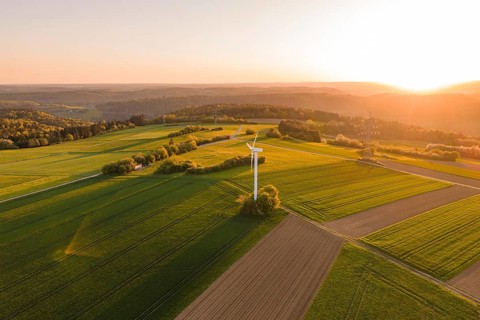 Wide green fields with a single wind turbine, brilliant sunset, hilly landscape in the background,