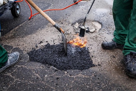 Road workers repair a pothole on a street by pouring hot asphalt from a bag and smoothing it with a