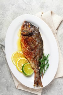 Baked dorado fish, in the oven, fried dorado, with spices and herbs, on a white plate, top view,