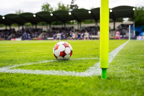 Football resting near the corner flag on a green pitch before a set piece during a soccer match in