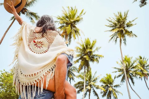 Happy young couple piggyback walking having fun on sandy pathway under tall coconut palm trees