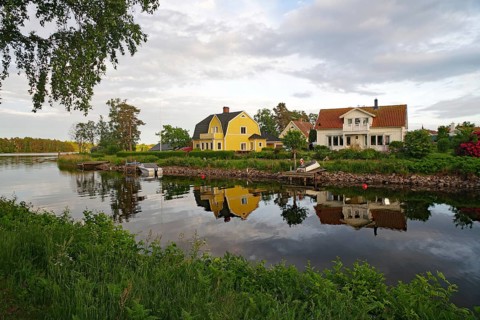 Two colorful houses by the river with a clear reflection in the water, surrounded by green nature