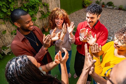 Diverse people standing outdoors in a circle, smiling and clapping hands enthusiastically,