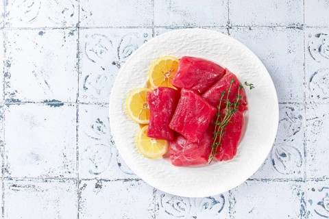 Fresh tuna slices, on a white plate, with lemon slices and herbs, top view, no people