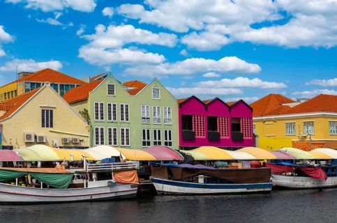 Traditional boats at the floating market in front of vibrant colonial architecture in the Punda