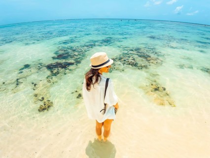 Tourist Woman on vacation standing at shoreline facing turquoise Indian Ocean on Zanzibar south