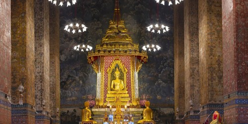 Golden meditating Buddha surrounded by wall paintings with Buddhist teachings and representations