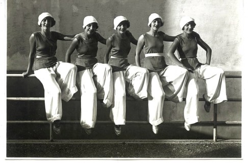 Five woman in 1920s-style clothing are sitting casually on a railing and laughing, the 1920s,