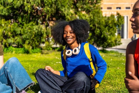 Young diverse students sitting on campus lawn on a sunny day, smiling and relaxing together between