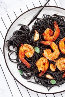 Black spaghetti with shrimp, on a white plate with a fork, on a striped napkin, marble background,