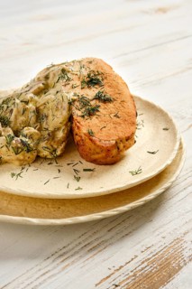 Grilled meat served with creamy mushroom sauce and herbs on simple plate at kitchen table