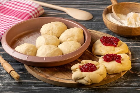 Dough pieces filled with marmalade in and next to the baking pan