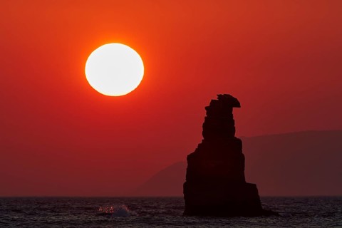 Red sunset casts an intense light on the sea and a solitary rock, sunset, South of the Amari Basin,