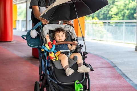 Father walks with baby son in stroller under umbrella on sunny city sidewalk, sharing protective,