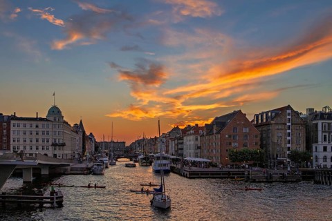 Farbenfroher Sonnenuntergang über einer Stadt mit Kanal und Booten unter einem dramatischen Himmel,