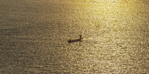 Fisherman with longtail boat (Thai: Ruea Hang Yao) at sunrise, Mekong between Thailand and Laos