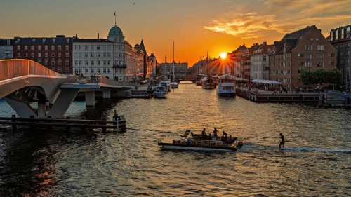 Sonnenuntergang über einer Stadt mit Brücke, Booten und einem leuchtenden goldenen Himmel,