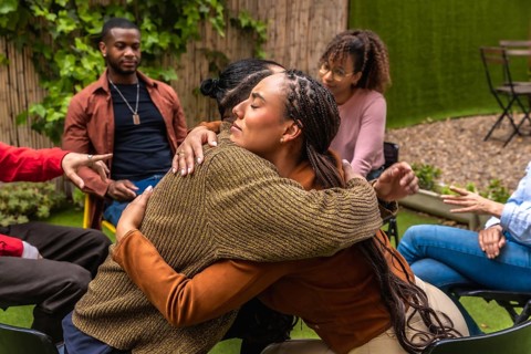 Diverse adults in an outdoor support circle offering empathy, hugs and active listening during