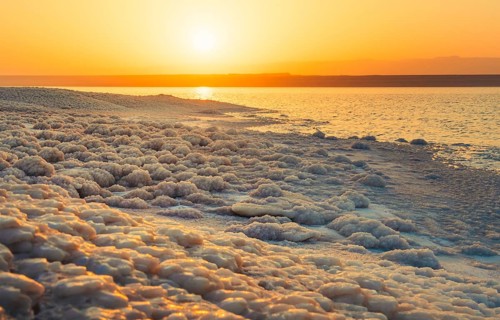 Close up Dead Sea salt crystals on shoreline beach in Jordan at sunset with turquoise water desert