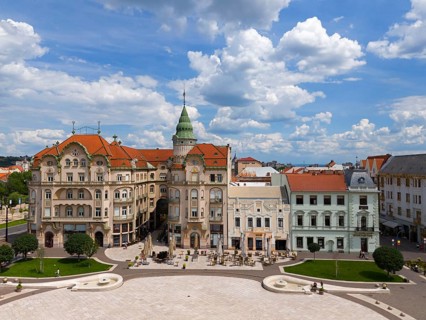 Baroque series of buildings with green dome and red roofs surrounding a square in a city, aerial