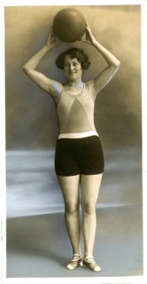 Swimwear, England, woman in swimsuit holding a ball over her head and posing in studio,