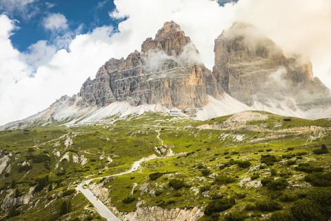 Aerial caravan of vehicles drive with cyclist riding uphill to Tre Cime di Lavaredo. Massive