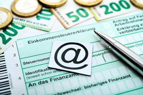 At sign on income tax return with banknotes and coins, symbolic photo digital income tax return +++