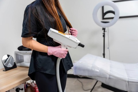 Medical specialist in pink gloves holds a modern laser device over a clinic table, preparing for a