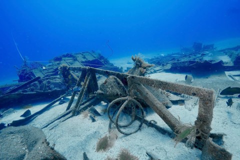 An old shipwreck lies on the seabed surrounded by sand and clear blue water, meteor wreck dive
