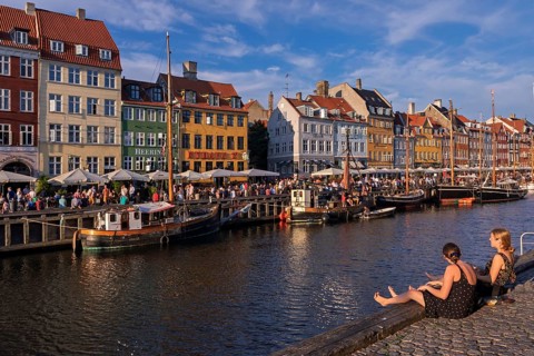 Lebendiges Treiben entlang eines Kanals mit bunten Häusern und Booten bei Sonnenschein, Kopenhagen,
