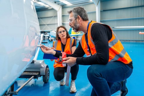Aviation engineers crouching on the hangar floor, meticulously inspecting the small aircraft's
