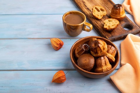 Golden caramelized Canele cookies dessert, cup of coffee, on blue wooden background with orange