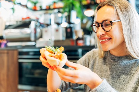 Smiling Woman Holding a Bao Bun with Fresh Ingredients in a Modern Cafe