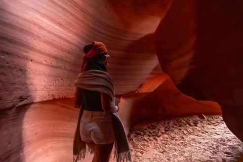 Woman standing inside a slot canyon, admiring the natural geological formations of sandstone walls