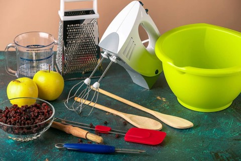 Kitchen utensils, mixer, grater, bowl next to apples and raisins on a table