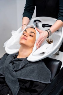 Woman with closed eyes relaxed at a salon basin as hairdresser shampoos and massages her hair,