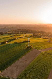 Wide green fields with a wind turbine, under brilliant sunset, gently rolling hills in the