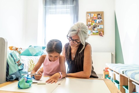 Grandmother attentively assisting her young granddaughter with schoolwork and studying at a desk in
