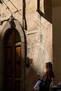 Woman leaning against a house wall with drink and shopping bag, Florence, Tuscany, Italy